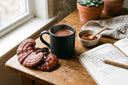 Tasse de cacao chaud au reishi, champignons reishi (Ganoderma lucidum) laqués rouges et bol de poudre de reishi sur un bureau en bois, à côté d'un carnet de suivi bien-être